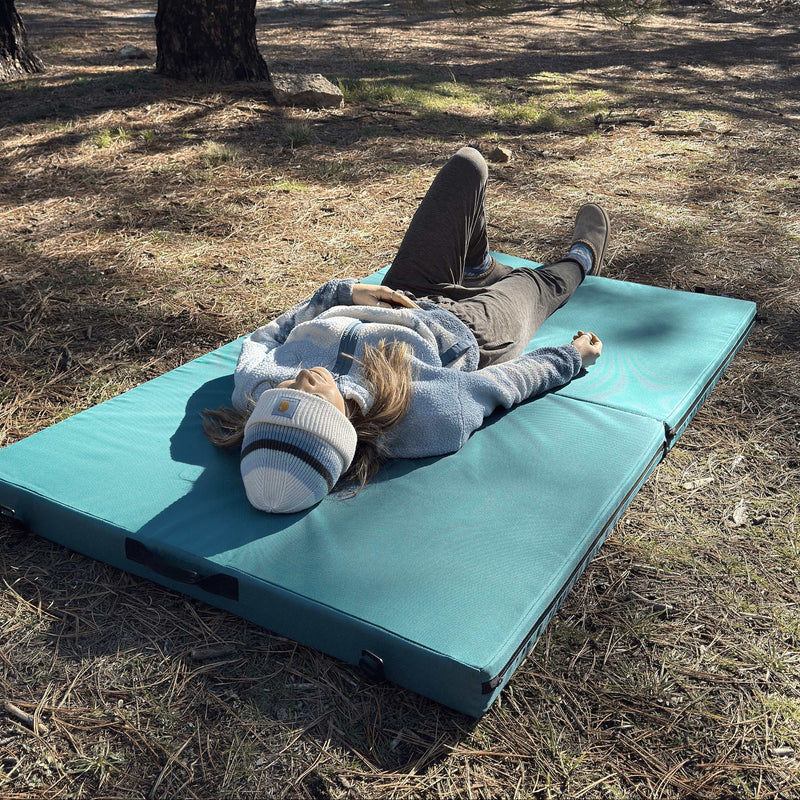 Person lying on a blue mat in a forest setting
