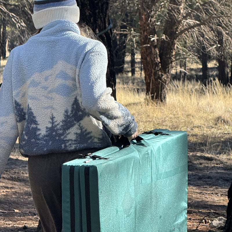 Person in winter clothing holding a stack of green mats outdoors.